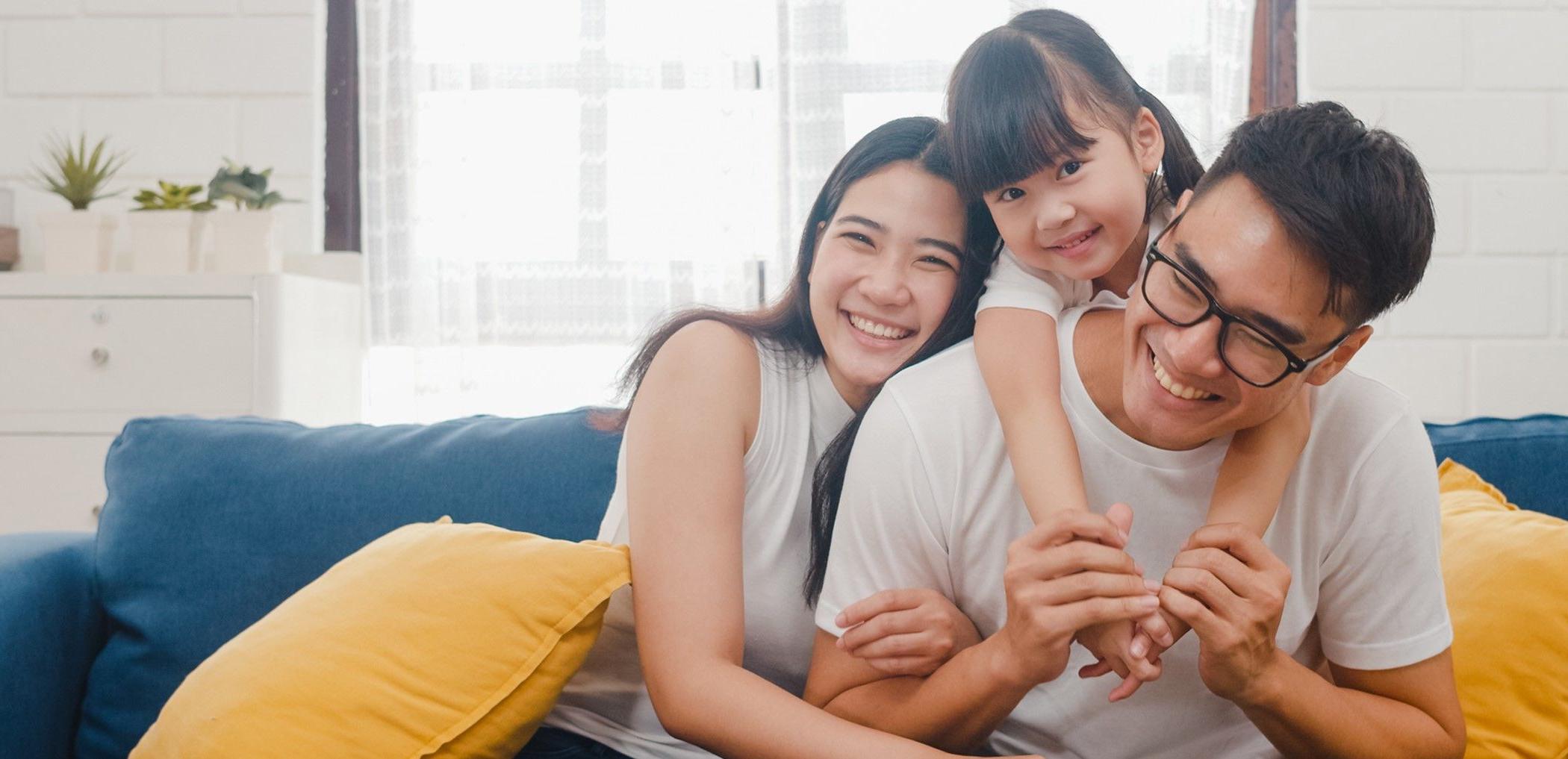 A little girl climbs up onto her young dad's back as mom smiles.